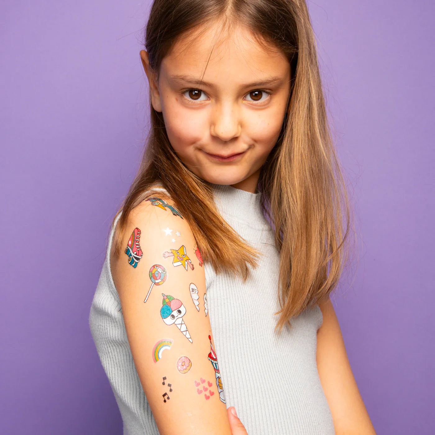 Young girl with colorful temporary tattoos on her arm against a purple background