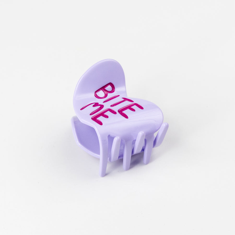 Purple heart-shaped hair claw with 'BITE ME' text on a white background
