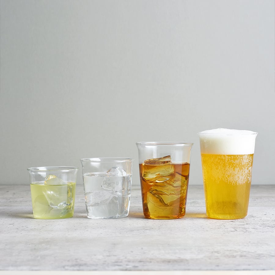 Five glasses with different beverages on a light wooden surface and gray background