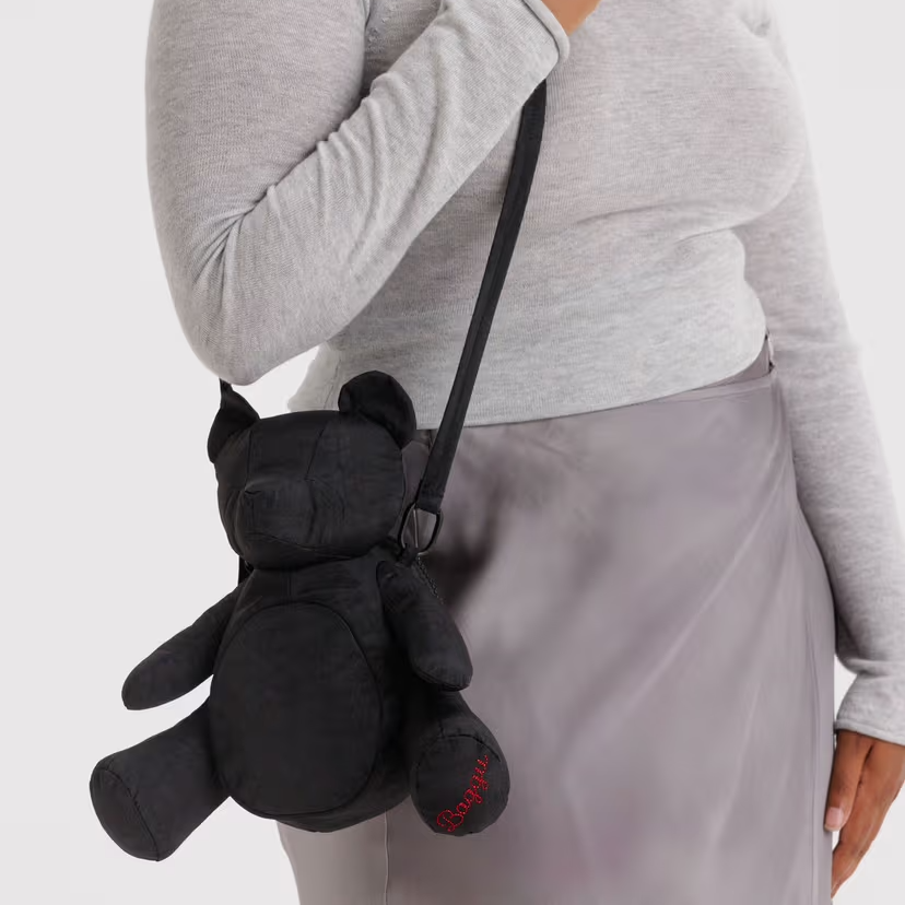 Person wearing a gray sweater and light gray skirt with a black teddy bear-shaped bag over their shoulder.