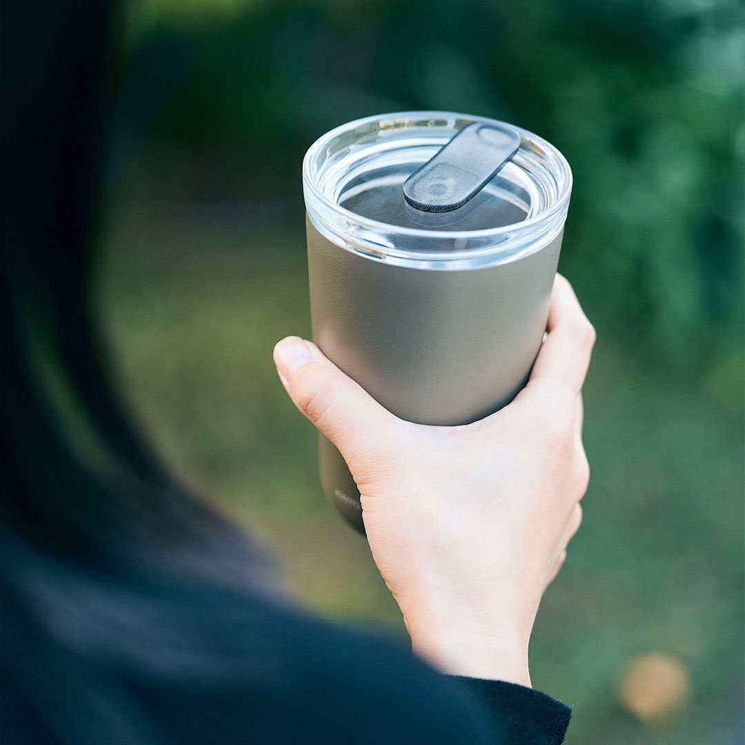 Hand holding a gray insulated tumbler with a blurred green background