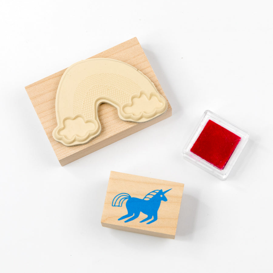 Two wooden stamps with cloud and unicorn designs, one with red ink pad, on a white background.