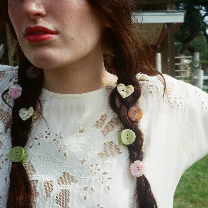 Person with braided hair adorned with colorful buttons in an outdoor setting