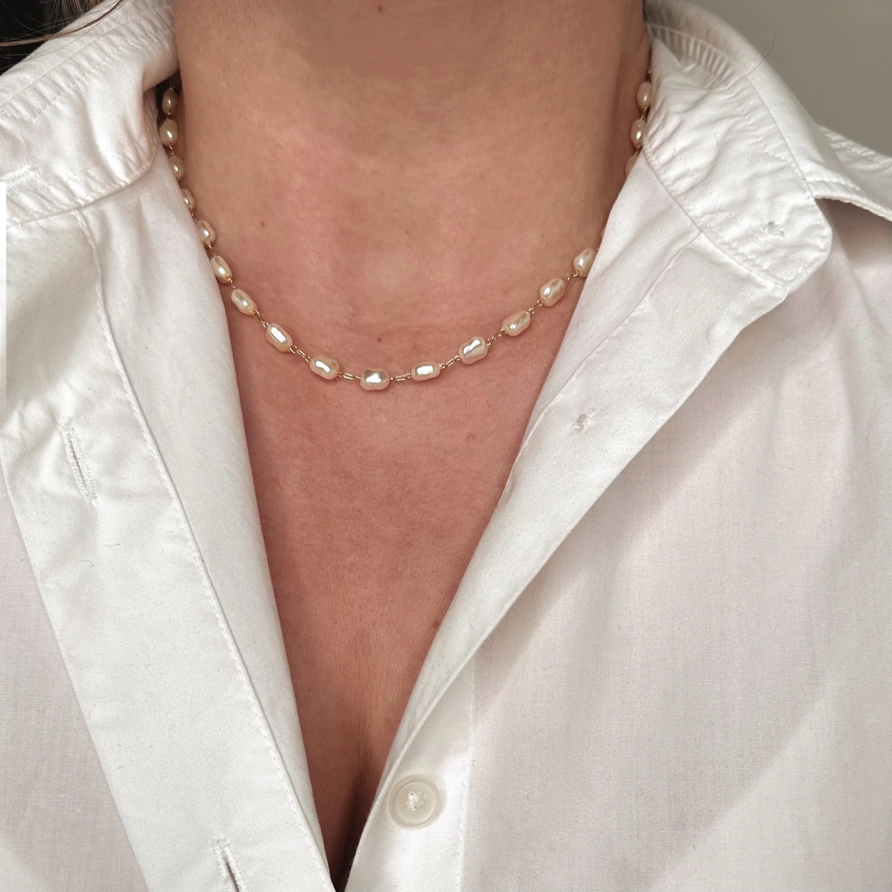 Pearl necklace worn by a person wearing a white shirt.