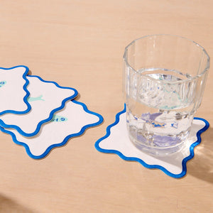 Coasters with blue scalloped edges on a wooden surface with a glass of water.