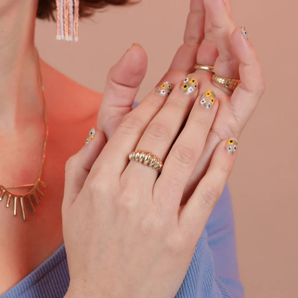 Close-up of hands wearing gold rings with decorative stones against a neutral background