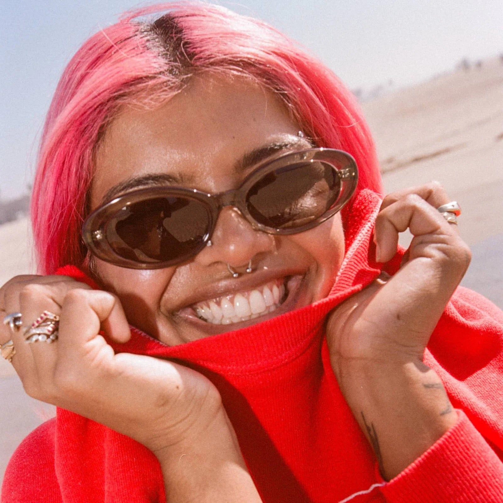 Person with pink hair wearing sunglasses and a red outfit, outdoors.