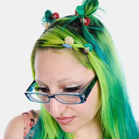 Person with green and blue hair styled in pigtails with decorative clips, wearing glasses.