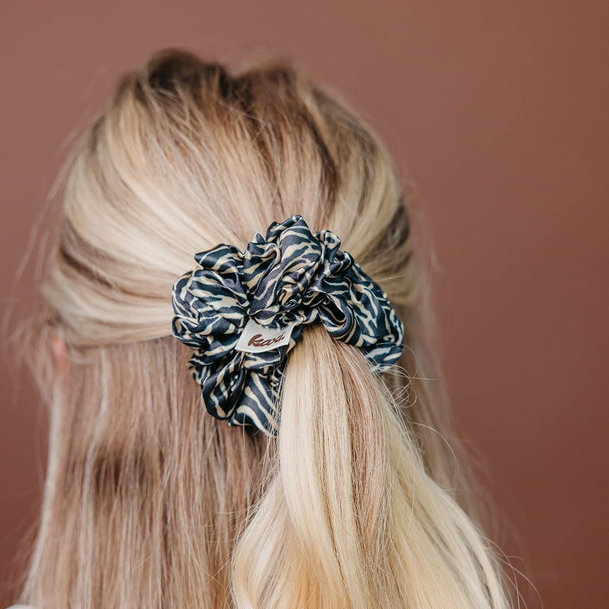 A black and beige zebra-print fabric scrunchie with a small white brand tag that reads 'box', shown on a plain light gray background.