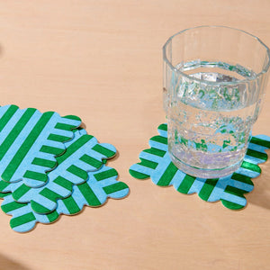 Set of green and blue striped coasters with a glass of water on a beige surface