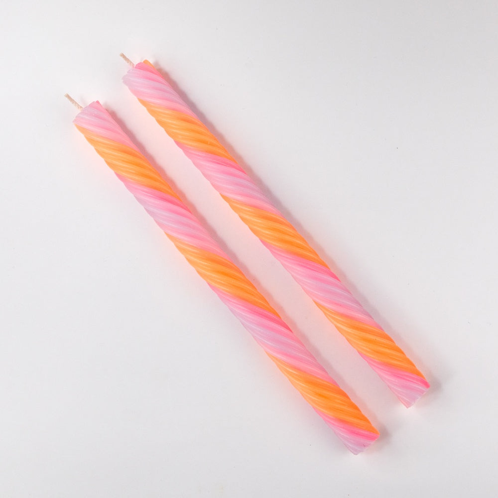 Three spiral-shaped candles in pink, orange, and white on a light gray background
