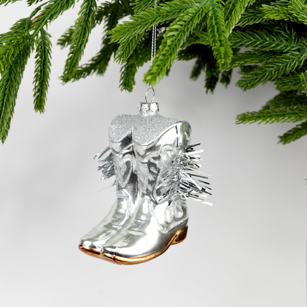 Silver cowboy boot ornament hanging on a Christmas tree branch.