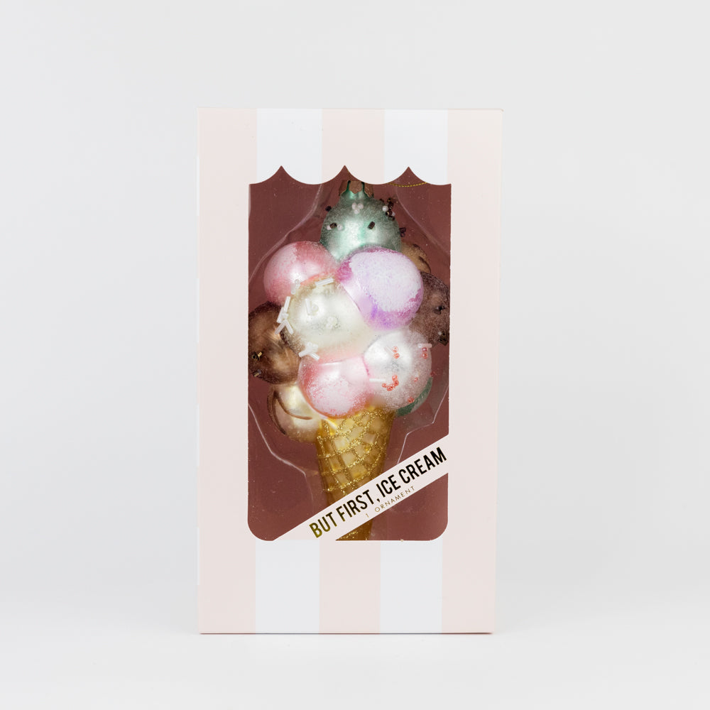 Small tree ornament of an ice cream cone with colorful toppings in a clear packaging box on a light pink background.