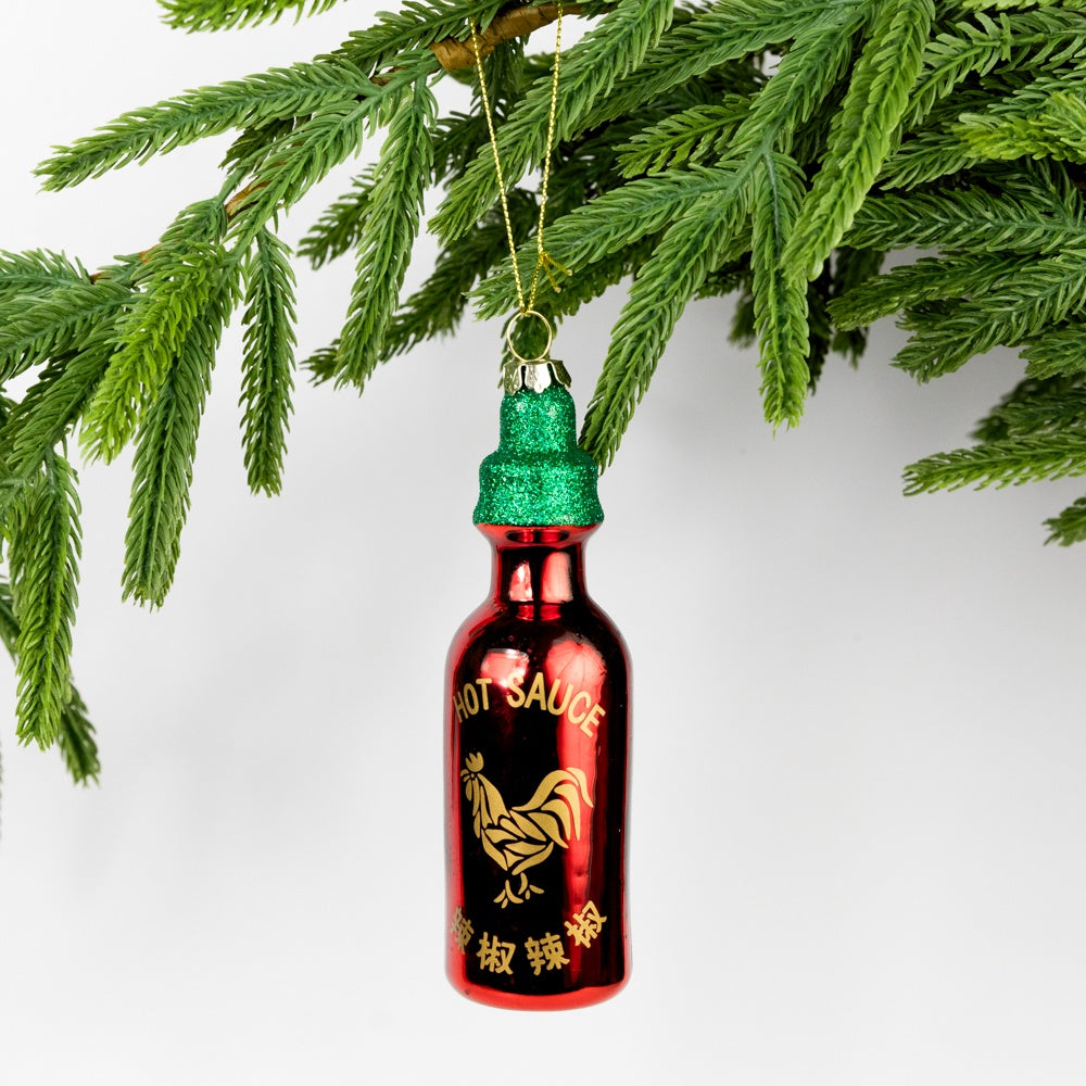 Hot sauce bottle ornament with green cap hanging on a Christmas tree branch.
