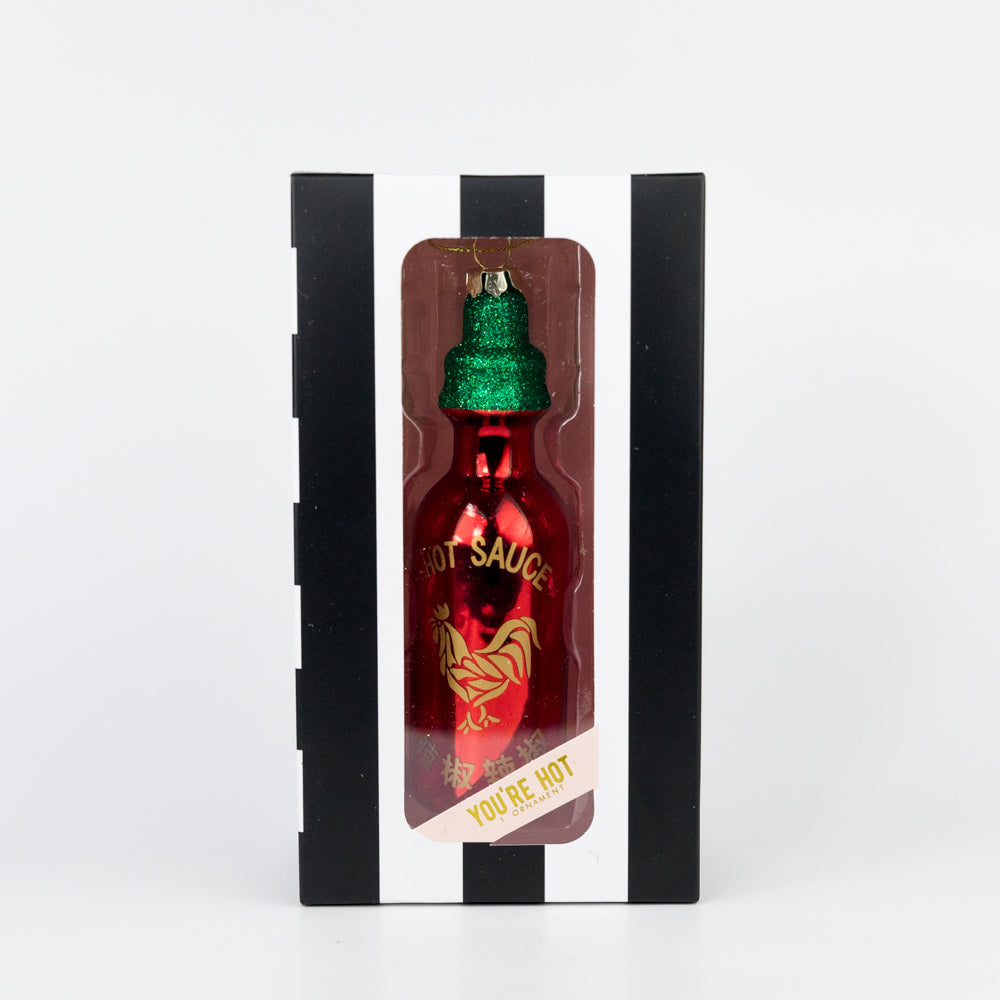 Decorative hot sauce bottle ornament with green cap in a black and white striped box on a white background
