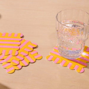 Yellow and pink striped coasters on a beige surface with a glass of water.