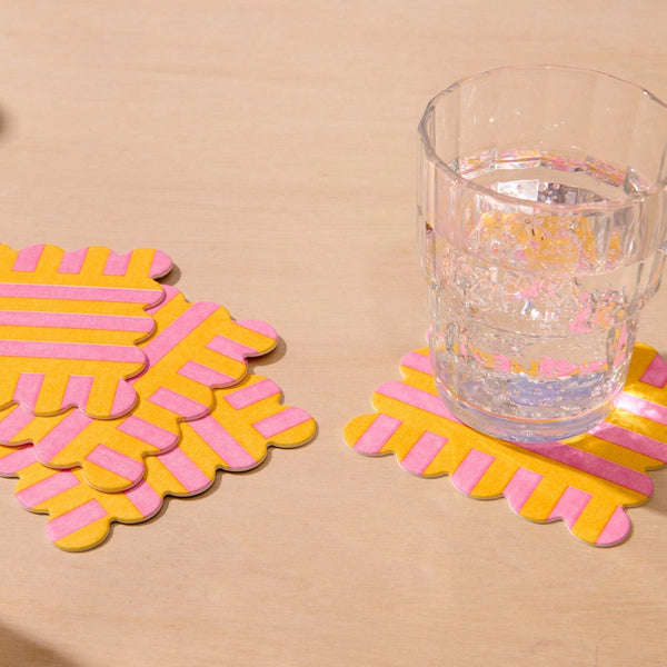 Yellow and pink striped coasters on a beige surface with a glass of water.