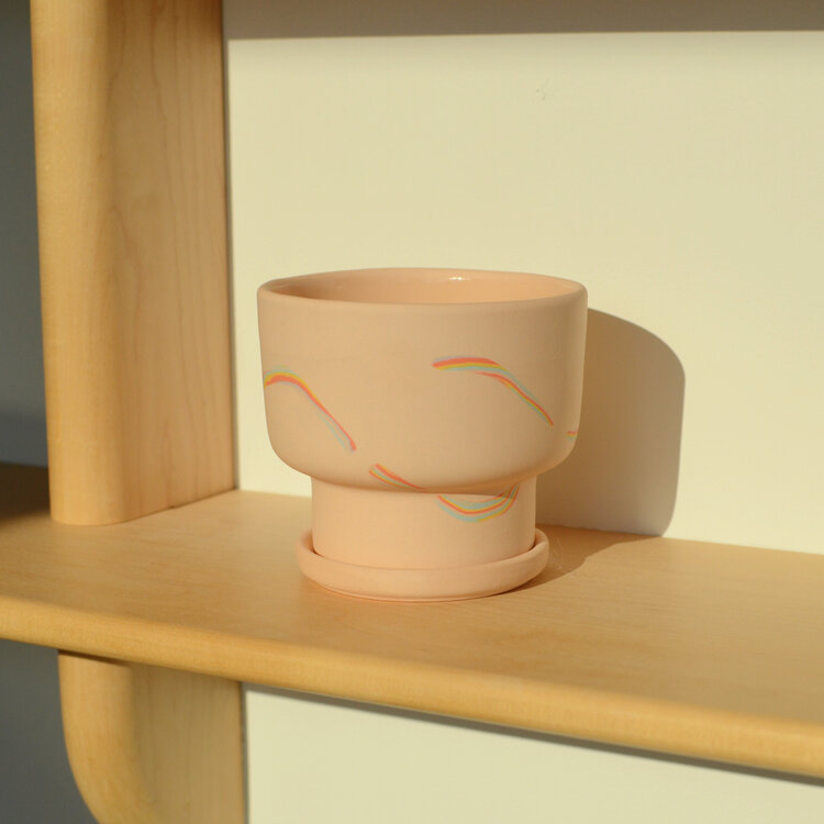 Pink ceramic planter with rainbow patterns on a wooden shelf