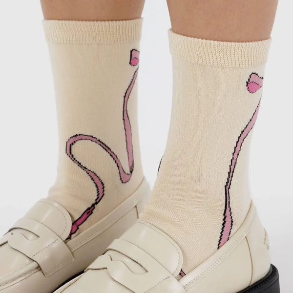 Beige loafers with pink bowdesign socks on a white background