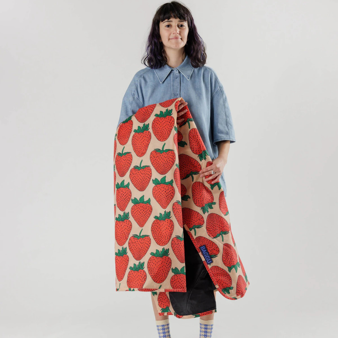 Person holding a strawberry-patterned blanket against a plain background