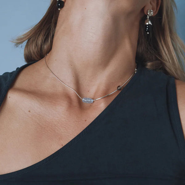 Close-up of a woman wearing a necklace and earrings against a blue background