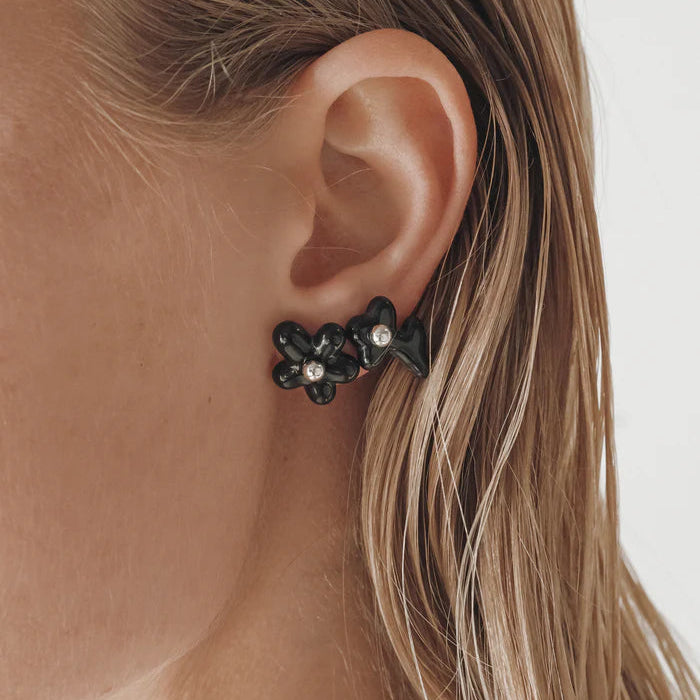 Close-up of an ear wearing a black floral earring with clear stones.