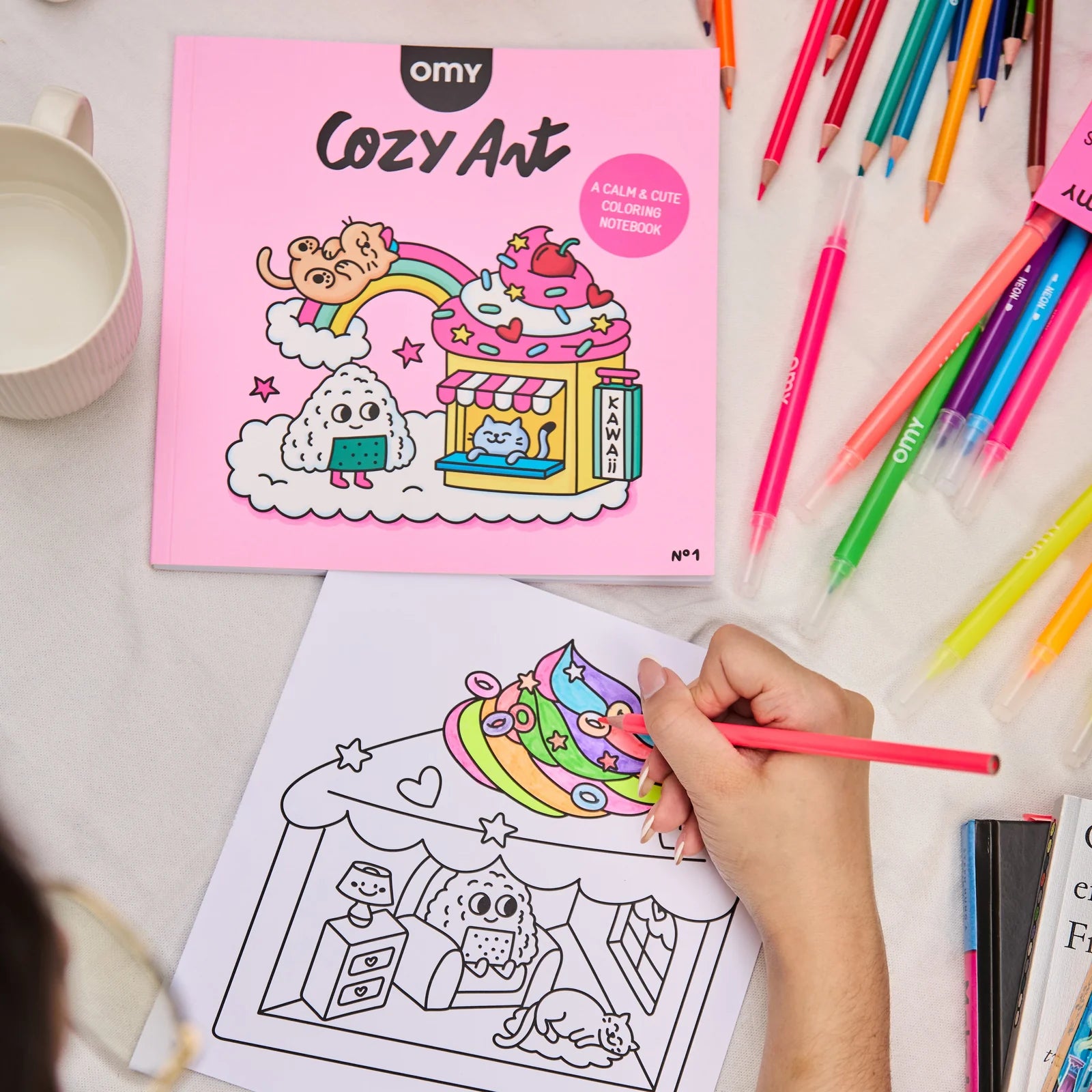 Coloring book titled 'Cozy Art' with coloring page and colorful pencils on a table.