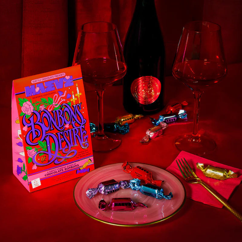 Box of Bonbons Devine chocolates with a bottle of wine and glasses on a red tablecloth.