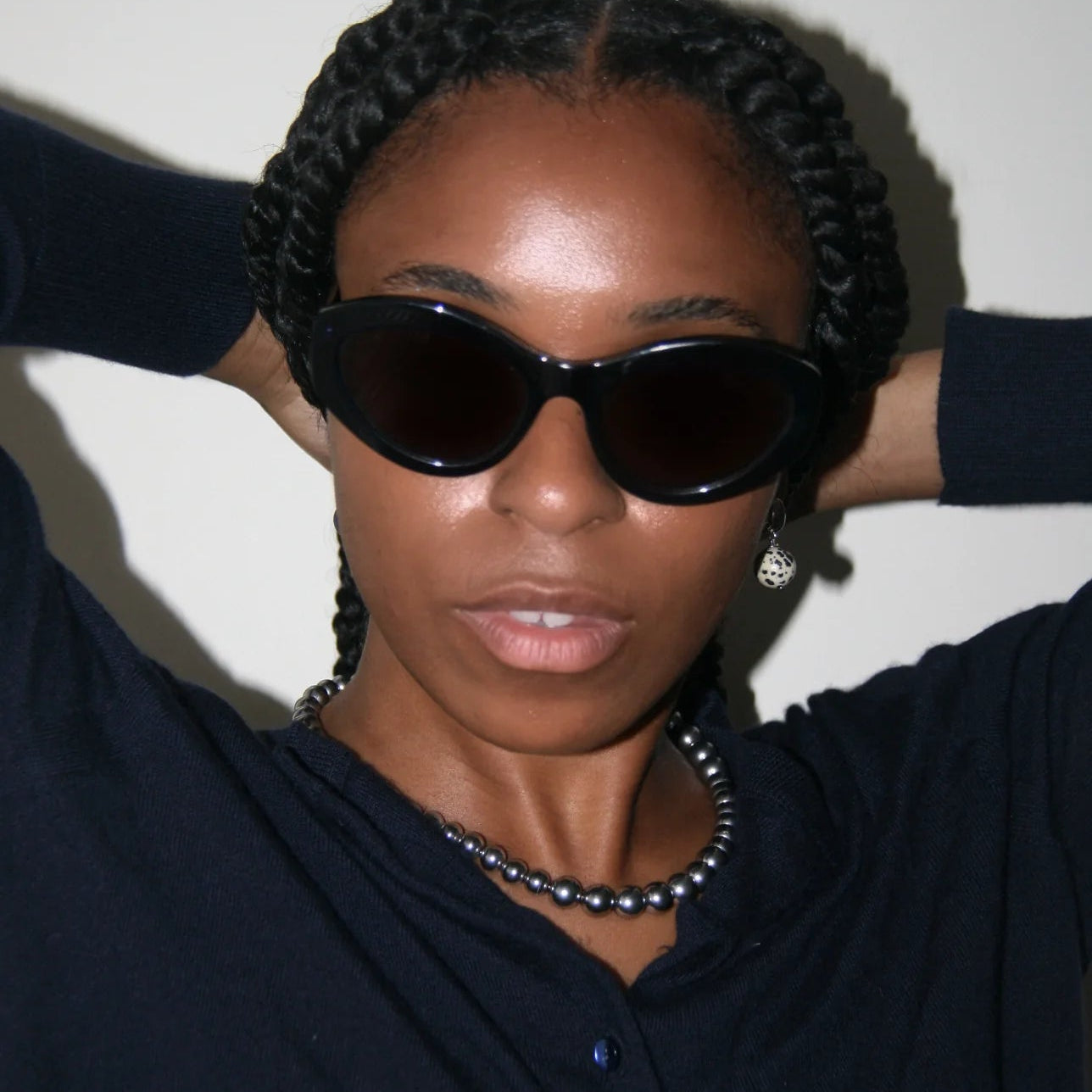 Person wearing sunglasses and a dark outfit against a plain background