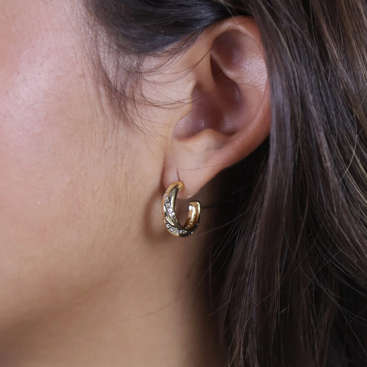 A pair of small gold crescent-shaped hoop earrings with a textured, hammered finish, displayed on a clean white background.