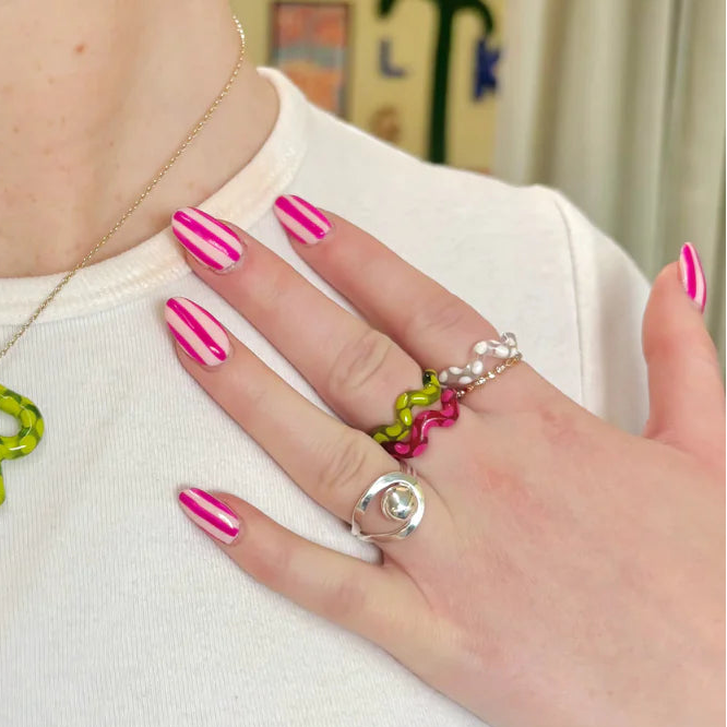 Hand with pink nail polish wearing multiple rings on a white background