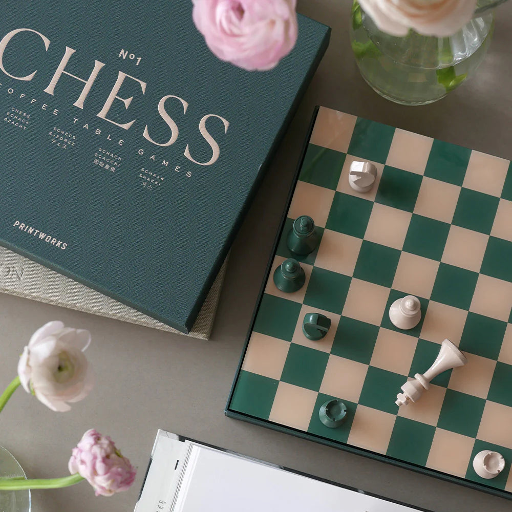 Chess set with pieces on a checkered board, surrounded by flowers and books.