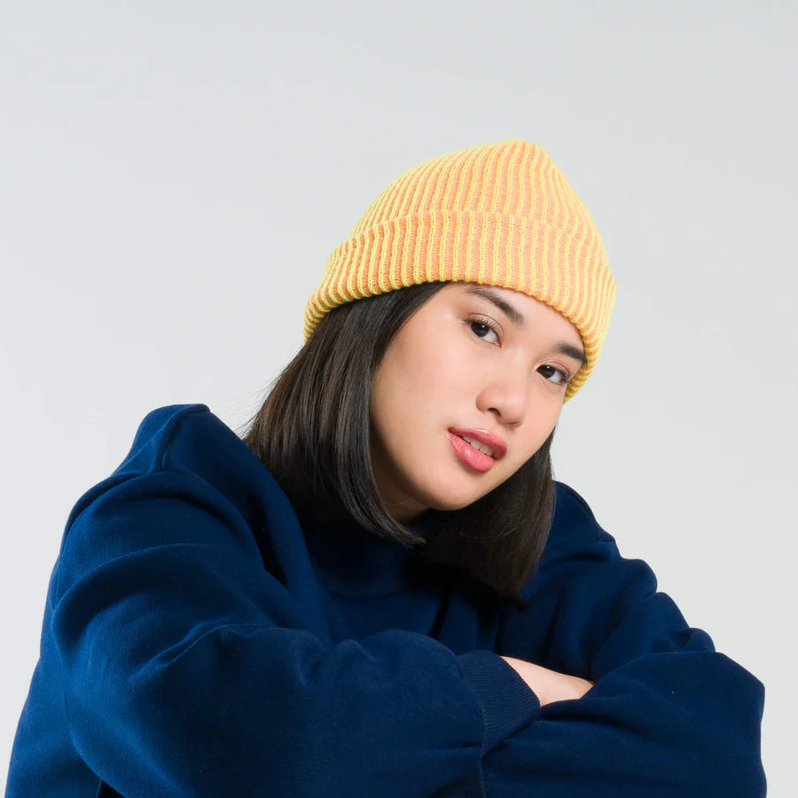 Person wearing a yellow beanie and blue hoodie against a light gray background