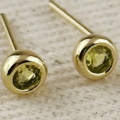 Gold earrings with green gemstones on a light background