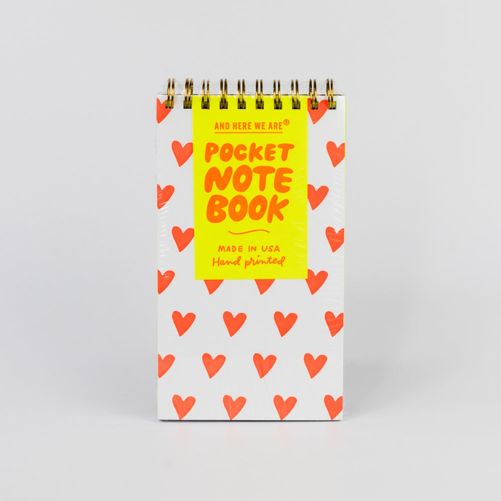 Pocket notebook with red heart pattern and yellow label on a light gray background