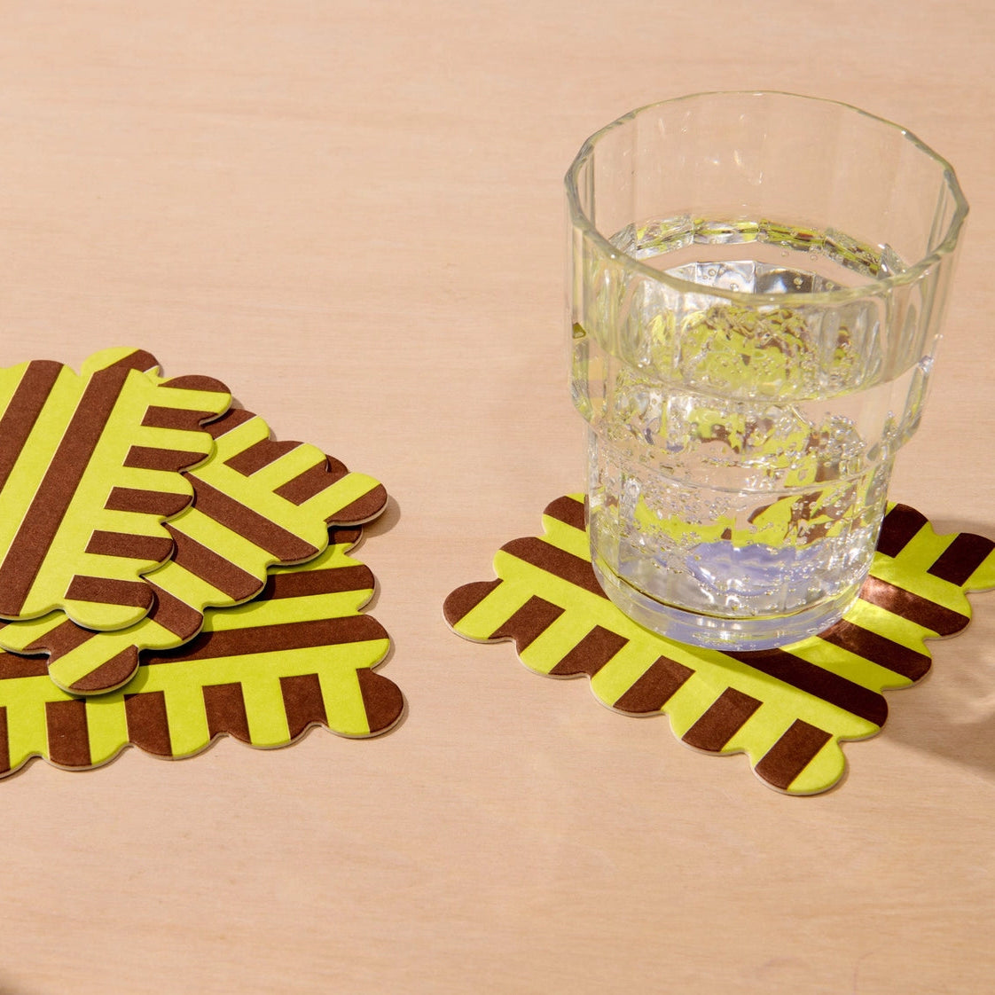 Set of striped coasters with a glass of water on a beige surface
