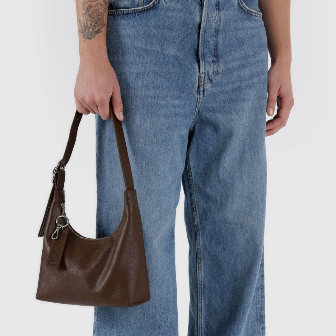 Brown leather handbag held by a person wearing blue jeans on a white background
