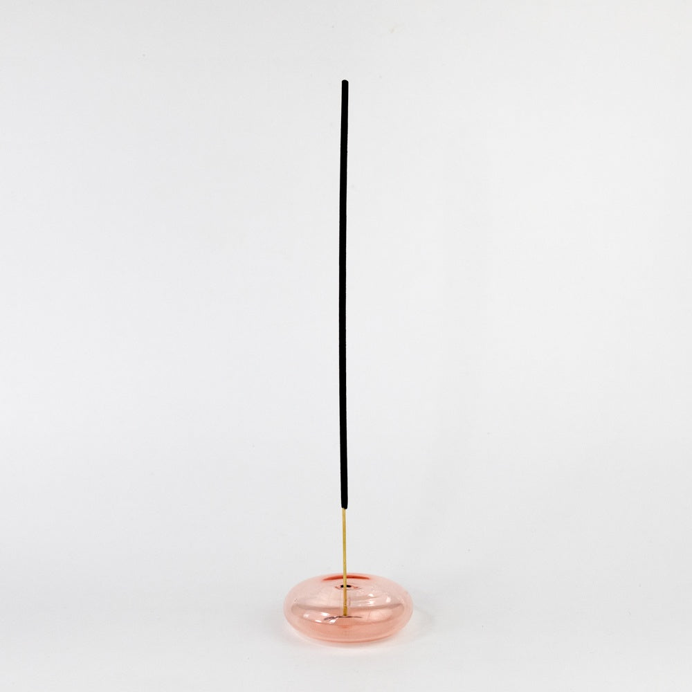 Incense stick in a coral colored glass holder on a white background