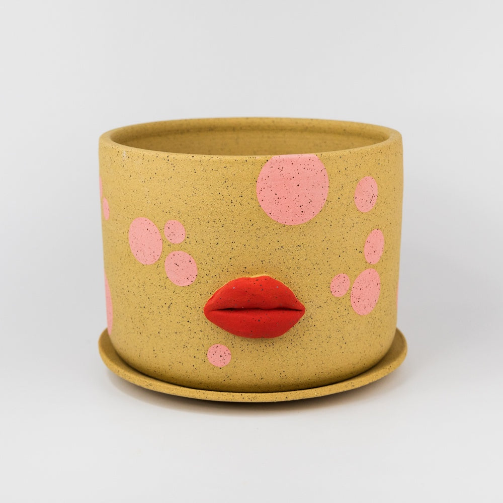 Yellow pot with pink polka dots and red lips on a white background