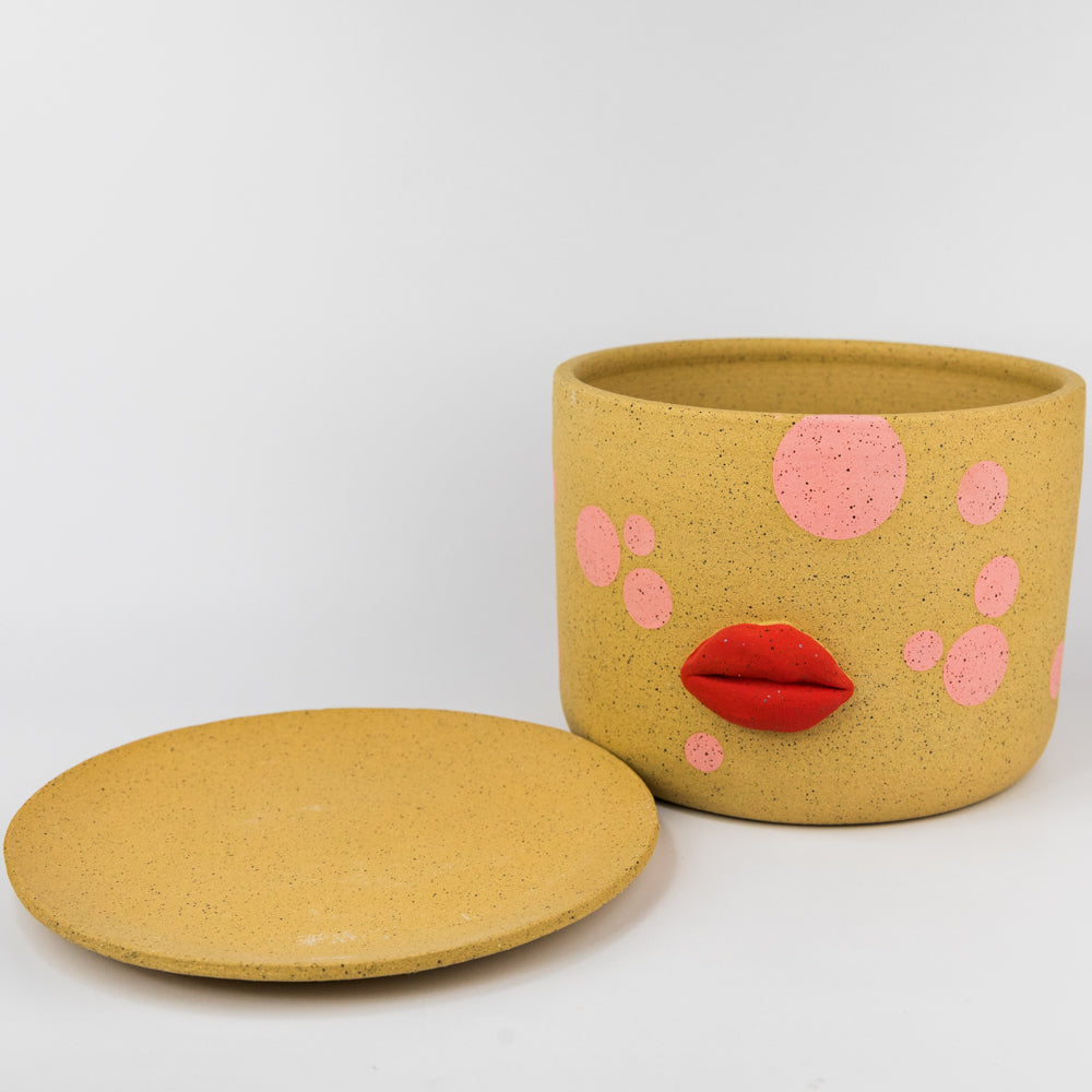 Yellow pot with pink polka dots and red lips on a white background