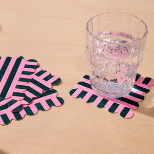 Pink and black striped coasters on a beige surface with a glass of water.