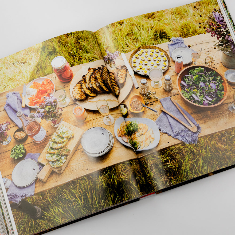 Open book showing a table with food and drinks on a grassy background