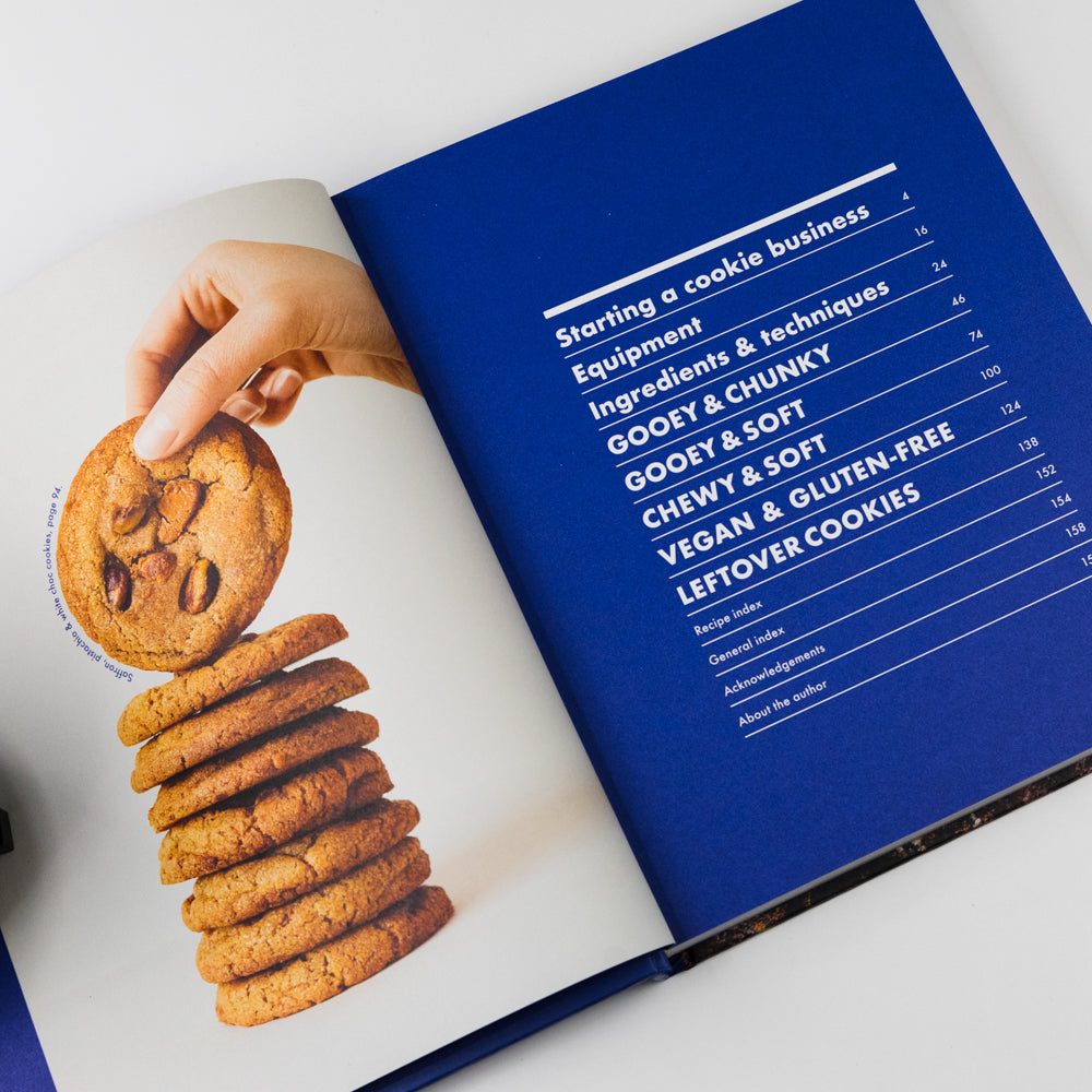 Open cookbook with a hand holding a cookie and a stack of cookies on a white background