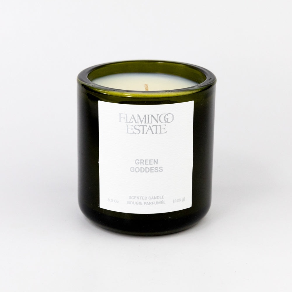 Candle in a green glass jar with a white label on a light gray background