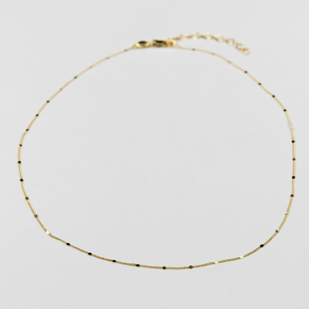 Delicate gold necklace with pressed details on a light gray background