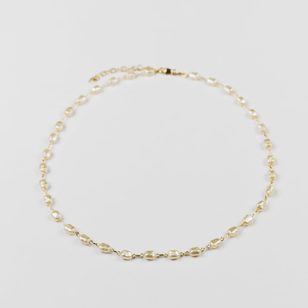 Gold necklace with small pearls on a light gray background