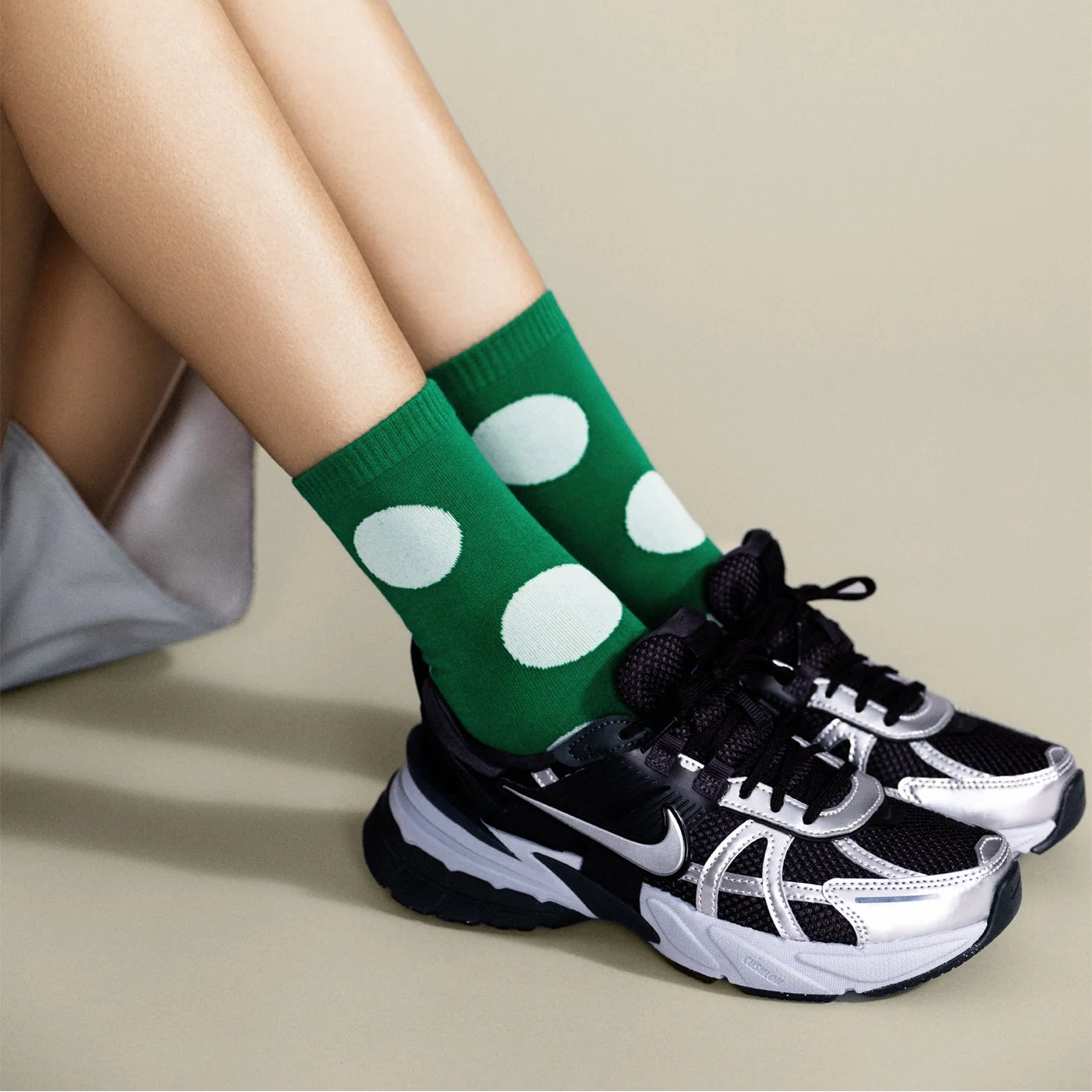 Green socks with white polka dots worn by a person sitting on a beige surface.