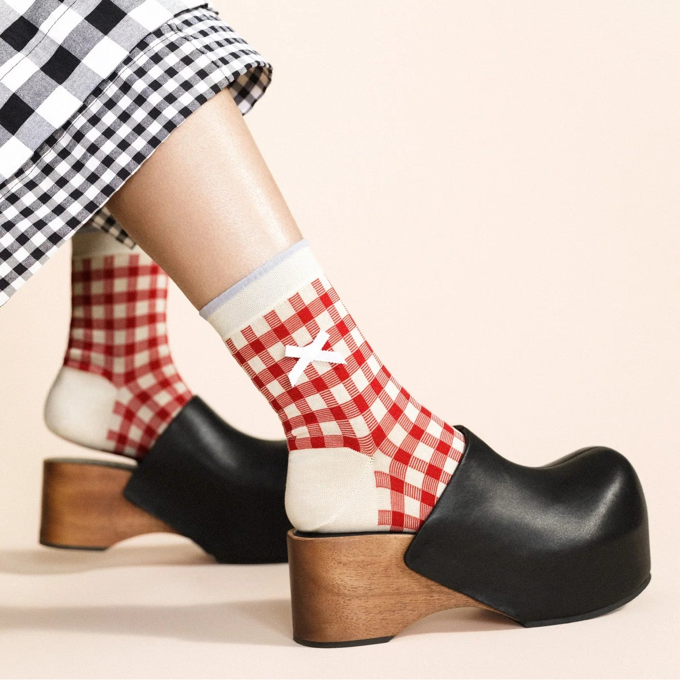 Person wearing red and white checkered socks with wooden clogs on a beige background