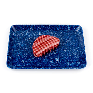 Rectangular blue speckled tray with a red hair claw on a white background