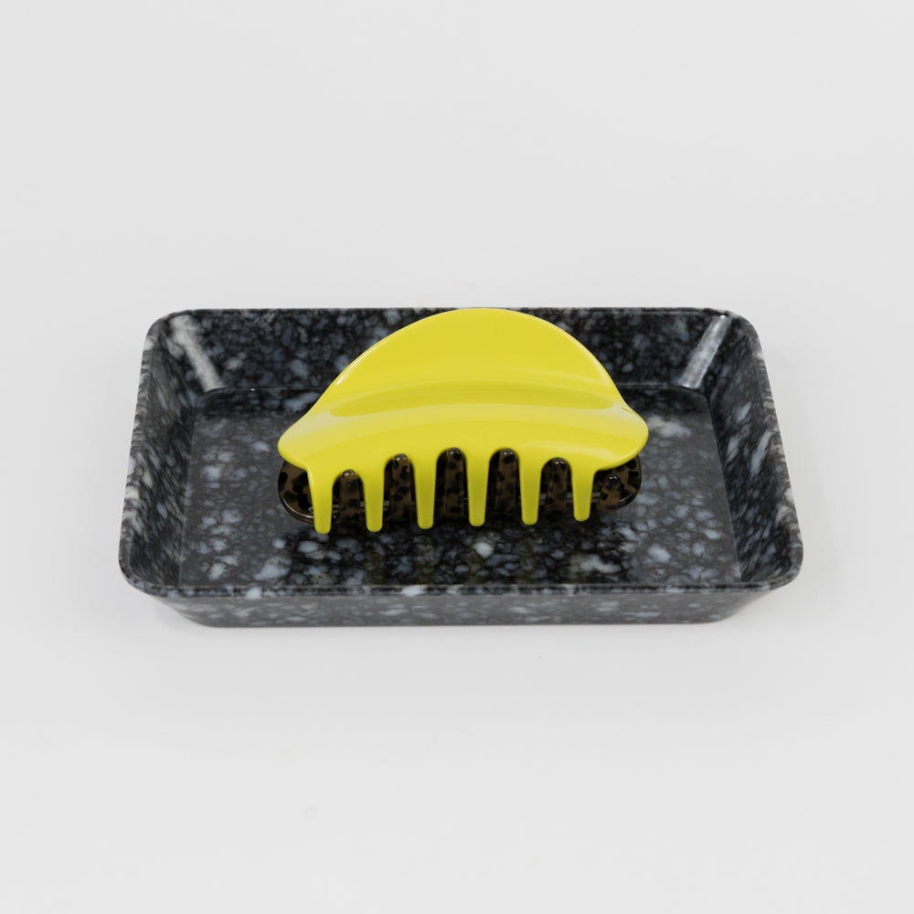 Yellow hairbrush on a black marble-patterned tray against a white background